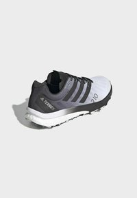 Zapatilla de running en negro y gris con parte superior sintética, diseño de tres rayas, suela acolchada y suela texturizada. Presenta un logo en el talón.