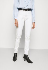 Jeans bianchi aderenti, a vita alta, con una texture liscia, abbinati a un top azzurro chiaro con dettagli arricciati e una cintura nera con una fibbia argentata.