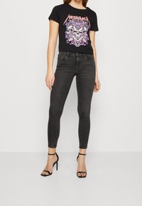 Black short-sleeve T-shirt with a graphic print of a skull surrounded by colorful designs, paired with dark gray skinny jeans and black strappy heels.