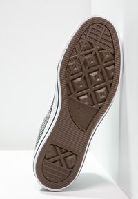 Suola in gomma nera con motivo a trama geometrica, caratterizzata da una intersuola di colore chiaro e una tomaia in canvas grigio testurizzato. Marchio Converse All Star visibile.