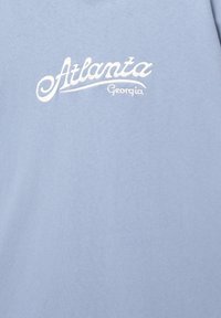 Light blue cotton t-shirt featuring white embroidered text reading "Atlanta Georgia" in a cursive font. Smooth texture, casual design.