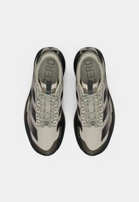 Beige und schwarze Sportschuhe mit schlankem Design, aus strukturiertem Stoff, mit runden Schnürsenkeln und gepolstertem Kragen. Sohle mit Grip-Akzenten.