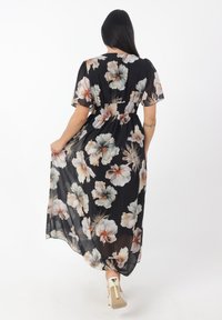 Robe maxi en tissu noir transparent avec un grand motif floral en crème et rose. Présente une taille smockée et des manches courtes et amples.