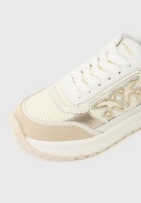 Ανοιχτό μπεζ και κρεμ αθλητικό παπούτσι με πλέγμα και σουέντ επάνω μέρος, επενδυμένη γλώσσα, επίπεδα κορδόνια και αντανακλαστικές ασημένιες λεπτομέρειες. Υφή από υφασμάτινη διακόσμηση.
