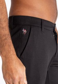Pantalones negros de tela lisa, con una sola raya y un pequeño diseño bordado multicolor cerca del bolsillo.