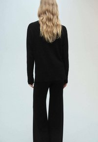 Crni pleteni pulover s opuštenim krojem, uparen s širokim crnim hlačama. Ima duge rukave i jednostavan, besprijekoran dizajn.
