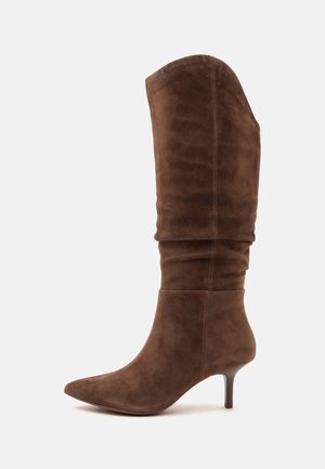 Botte haute en daim marron avec un bout pointu et un talon moyen étroit, présentant un design supérieur légèrement froissé.