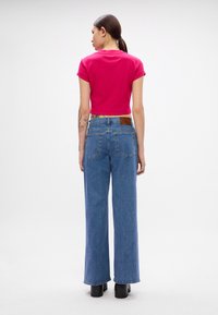 T-shirt rosa ajustado e cortado com jeans azuis de pernas largas, com um patch de couro castanho nas costas. Tecido suave e silhueta casual.