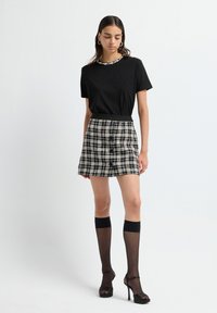 Camiseta negra de cuello redondo, falda mini de cuadros en blanco y negro, medias negras transparentes hasta la rodilla y tacones altos negros. Diseño y textura simples.