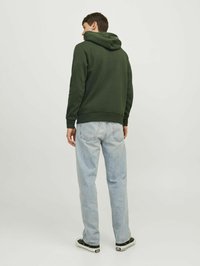 Sudadera de color verde oscuro con capucha, puños y dobladillo acanalados. Combinada con unos vaqueros de pierna recta de color azul claro y zapatillas negras con suelas blancas.