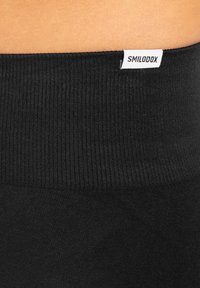 Zwarte geribbelde tailleband van leggings met een klein wit 'SMILODOX' label. Gladde textuur, aansluitend ontwerp, zichtbare stikseldetails.