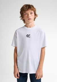 Bílá bavlněná tričko s černým logem na středu hrudi, kulatým výstřihem a krátkými rukávy. Jednoduchý design, hladká textura.