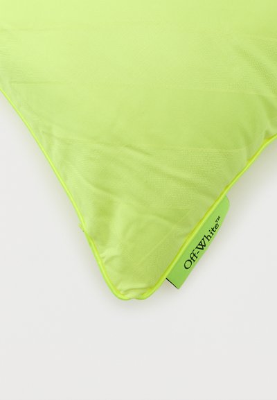 Γωνία τριγωνικού μαξιλαριού σε νέον κίτρινο-πράσινο με υφή υφάσματος και ετικέτα με το λογότυπο Off-White σε λευκό φόντο.