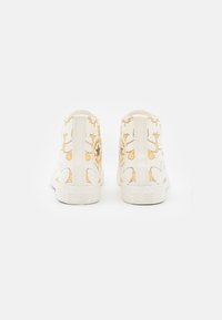 Hvide canvas høj-top sneakers med gule blomster mønstre, rundt logo-patch, tekstureret gummi sål og forstærket syning.