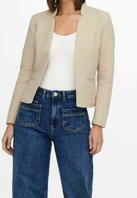 Blazer beige à finition texturée, fermeture à un bouton et encolure ronde, associé à un jean denim bleu foncé taille haute avec poches apparentes.