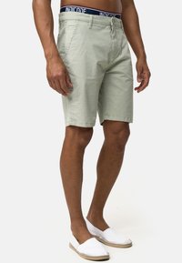 Hellgrüne Shorts mit Muster und strukturierter Oberfläche sowie einem dunkelblauen, elastischen Taillenbund. Kombiniert mit weißen Slippern.