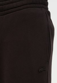 Μαύρο παντελόνι φόρμας από υφασμάτινη υφή με ελαστική μέση και πλαϊνές τσέπες· διαθέτει ένα μικρό, κεντημένο λογότυπο σε τόνο που ταιριάζει.