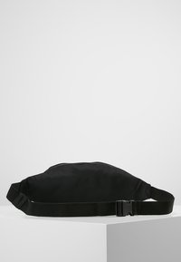 Svart nylon midjeväska med justerbar rem och plastspänne i sidan, visad mot en enkel vit bakgrund.