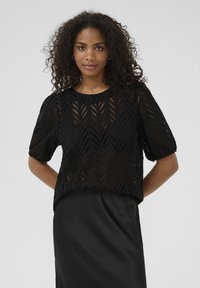 Haut noir à manches courtes avec un motif de feuilles en œillets, présentant un col rond et des manches bouffantes amples. Tissu lisse en dessous.