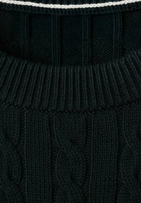 Nærbillede af en mørkegrøn sweater med kabelstrik og ribbet tekstur samt en tynd hvid stribe nær den øverste kant.