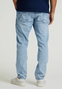 Hellblaue Denim-Jeans mit schmalem Schnitt, ausgestattet mit Gesäßtaschen mit dreieckigen Klappen und einer leicht verblassten Textur. Weiße Sneakers sind sichtbar.