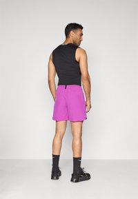 Men's athletic outfit featuring a sleeveless black top and bright purple shorts. Notable details include black branding and black athletic shoes.