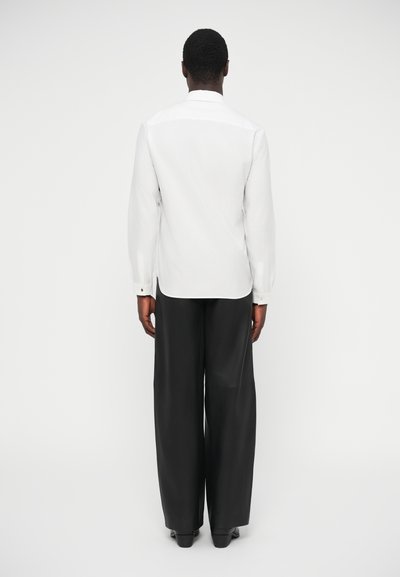 Chemise blanche à manches longues et pantalon noir ample, design minimaliste, texture lisse et col simple. Vue de dos présentée.