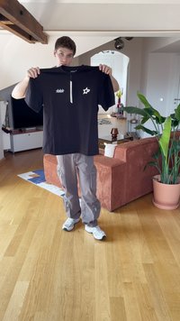 Černé tričko s krátkým rukávem a polo zipem, zdobené bílými hvězdami a logem. Nosené s šedými cargo kalhotami a bílými teniskami.