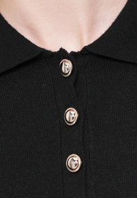 Gros plan sur un vêtement tricoté noir avec trois boutons métalliques ronds et brillants et un col plié au niveau de l'encolure.