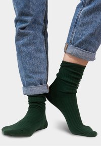 Zielone skarpetki w prążki o miękkiej strukturze, noszone z podwiniętymi niebieskimi dżinsami, które podkreślają wysokość i dopasowanie skarpet.