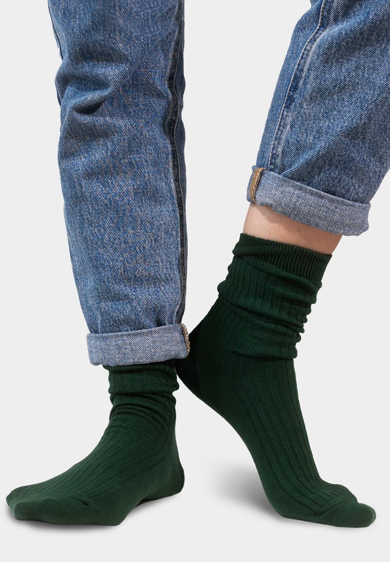 Zielone skarpetki w prążki o miękkiej strukturze, noszone z podwiniętymi niebieskimi dżinsami, które podkreślają wysokość i dopasowanie skarpet.