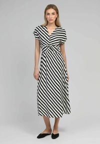 Robe striped en noir et blanc avec un décolleté en V, des manches courtes et un détail de taille noué. Longueur mi-mollet, avec une texture de tissu fluide.