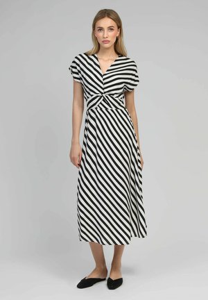 Robe striped en noir et blanc avec un décolleté en V, des manches courtes et un détail de taille noué. Longueur mi-mollet, avec une texture de tissu fluide.
