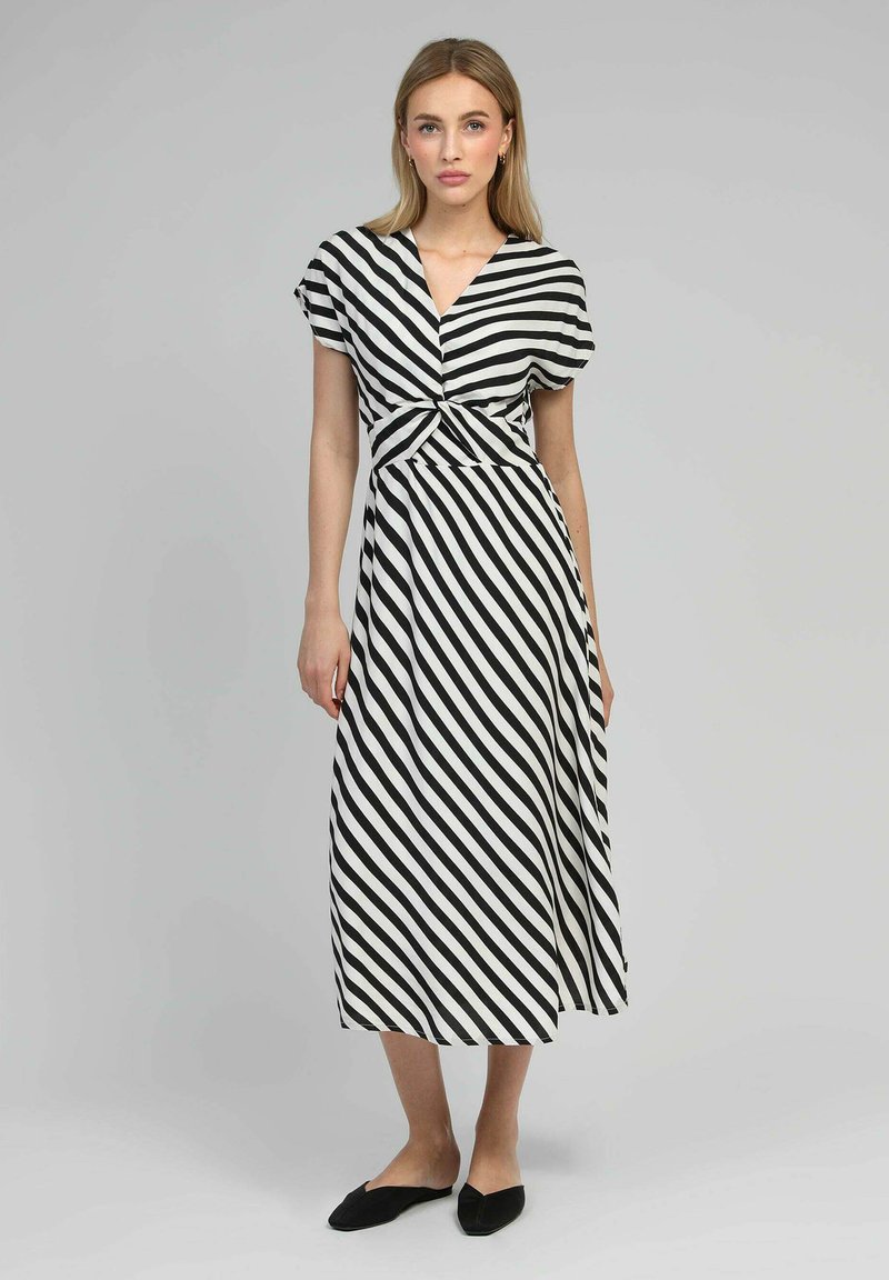 Robe striped en noir et blanc avec un décolleté en V, des manches courtes et un détail de taille noué. Longueur mi-mollet, avec une texture de tissu fluide.