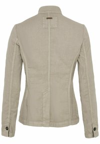 Beige tætsiddende jakke med lange ærmer, sømdetaljer, knaplukning ved manchetterne og en lille stoflap under kraven bagpå.