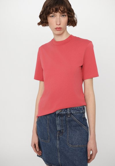 Coral cotton t-shirt with short sleeves and a round neckline. Worn with a blue denim skirt featuring pockets and a button closure.