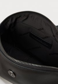 Melna kabata ar rāvējslēdzēju, atvērta, lai parādītu iekšējo auduma oderi ar atkārtotu "Karl Lagerfeld" zīmolu un mazu iekšējo kabatiņu.