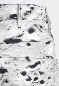 Jeansshorts med ett tryck av svart och vitt månlandskap, med en kraftig midja, synliga sömmar och flera fickor. Strukturerad tyg.