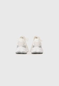 White athletic shoes with a textured mesh upper, silver accents, and a cushioned sole, featuring a minimalist design and laces at the back.