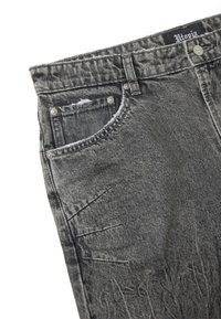 Jeans de mezclilla gris con un acabado desgastado, que presentan un diseño tradicional de cinco bolsillos, remaches y una etiqueta en la cintura. Cortes texturizados y de tiro medio.
