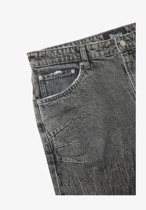 Jeans de mezclilla gris con un acabado desgastado, que presentan un diseño tradicional de cinco bolsillos, remaches y una etiqueta en la cintura. Cortes texturizados y de tiro medio.