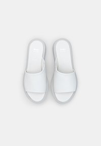 Bijele slip-on cipele s širokom trakom, gornji dio od mekanog kože i sivi gumeni potplat. Minimalistički dizajn, bez ukrasa ili uzoraka.