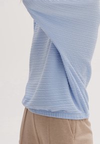 Jasnoniebieski sweter z teksturowanego dzianiny z prążkowanym wzorem, noszony na beżowych spodniach, z luźnym krojem i delikatnym opadaniem.