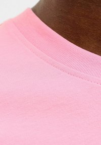 Camiseta de algodón rosa con cuello redondo acanalado. La tela tiene una textura suave y un color uniforme, mostrando un diseño sencillo y casual.