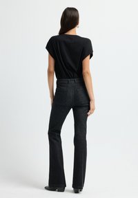 Zwarte top met korte mouwen gecombineerd met donkerdenim flare jeans. De jeans hebben achterzakken en een aansluitende taille. De stof is overal glad.