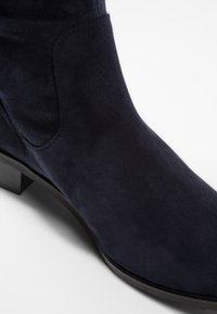 Stivale alla caviglia in suede blu navy con punta arrotondata e texture liscia, caratterizzato da un tacco basso e un delicato cucito lungo il lato.