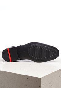 Semelle de chaussure en cuir noir avec un motif texturé, dotée d'un accent rouge au talon. Forme arrondie, finition lisse, construction robuste.