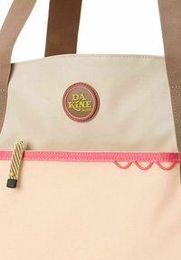 Borsa tote beige con manici marroni, un logo circolare, dettagli in cerniera rosa e anelli decorativi lungo il fondo. Materiale tessile resistente.