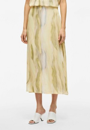 Larga y fluida falda de color amarillo pálido con patrones abstractos en verde y lavanda. La tela ligera tiene una textura suave. Mulees blancas de punta abierta.