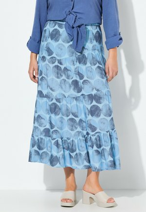 Falda azul de capas con grandes patrones circulares en diferentes tonos de azul. Tejido suave con un diseño fluido. Combinada con zapatos de color beige claro.
